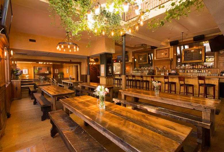 interior of a restaurant with large community-style tables, a long bar, and lots of wooden accents