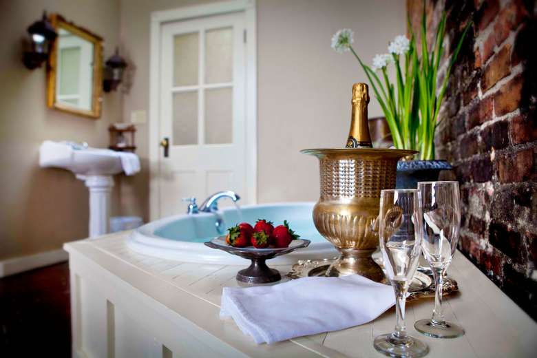 bottle of champagne, two glasses, and a tray of strawberries next to a soaker tub