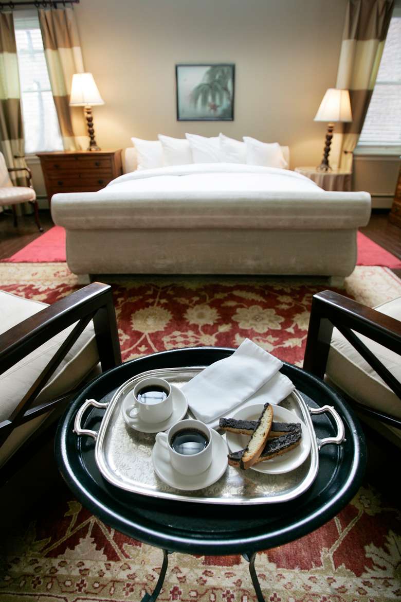 silver tray with two cups of coffee and a plate of biscotti with a king size bed in the background