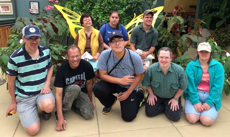 Eight people in a greenhouse surrounded by plants