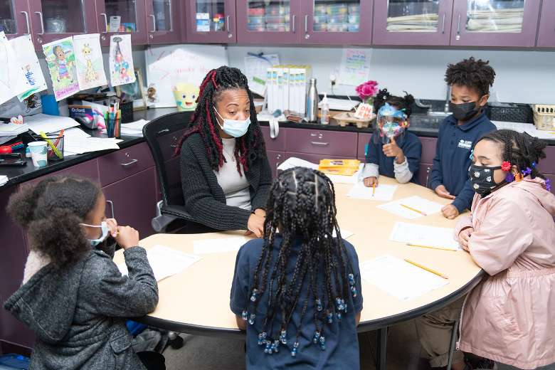 five students and a teacher at a small table in a classroom